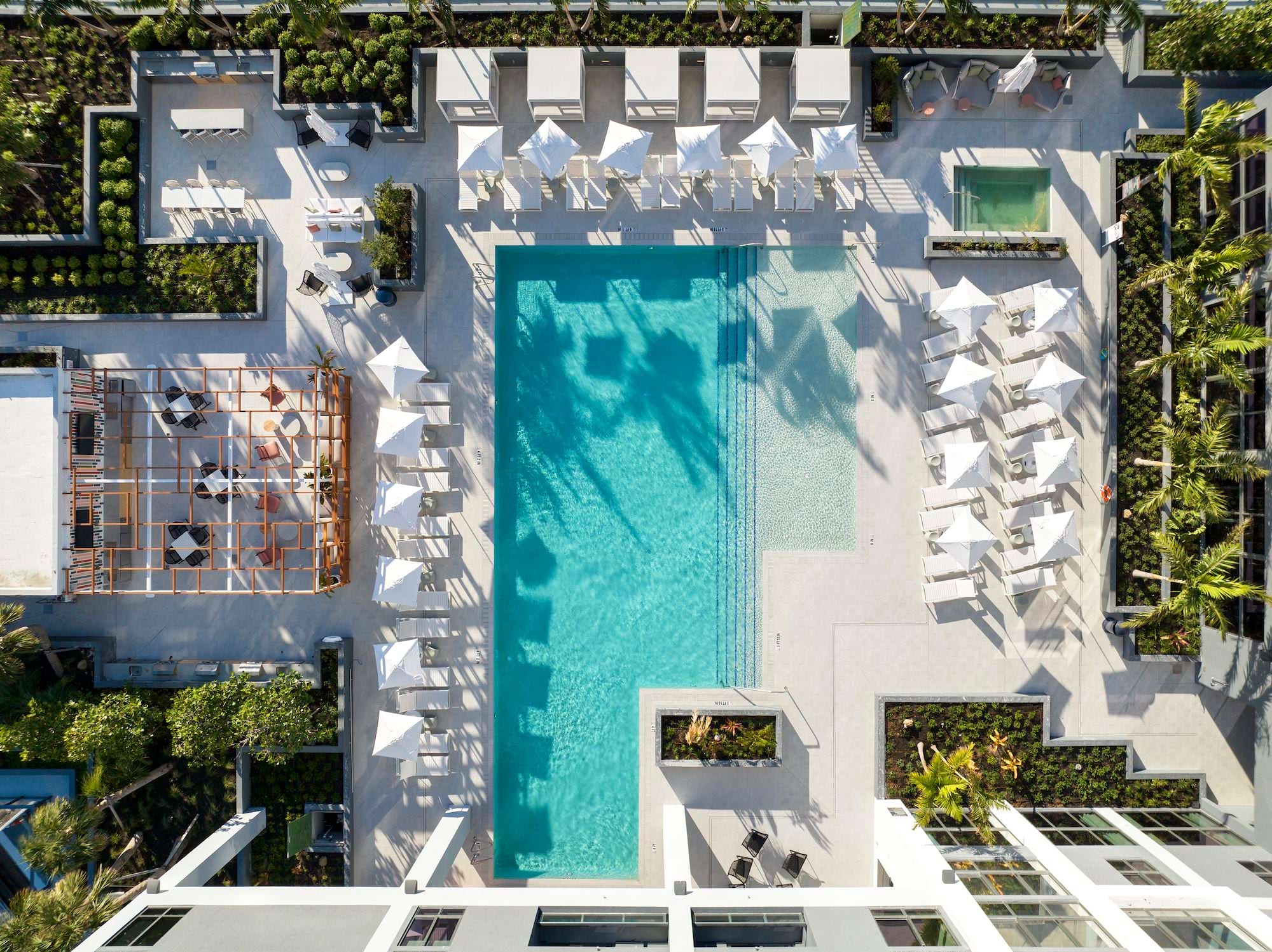 Overhead view of a luxury swimming pool area with lounge chairs, umbrellas, dining tables, and lush landscaping.